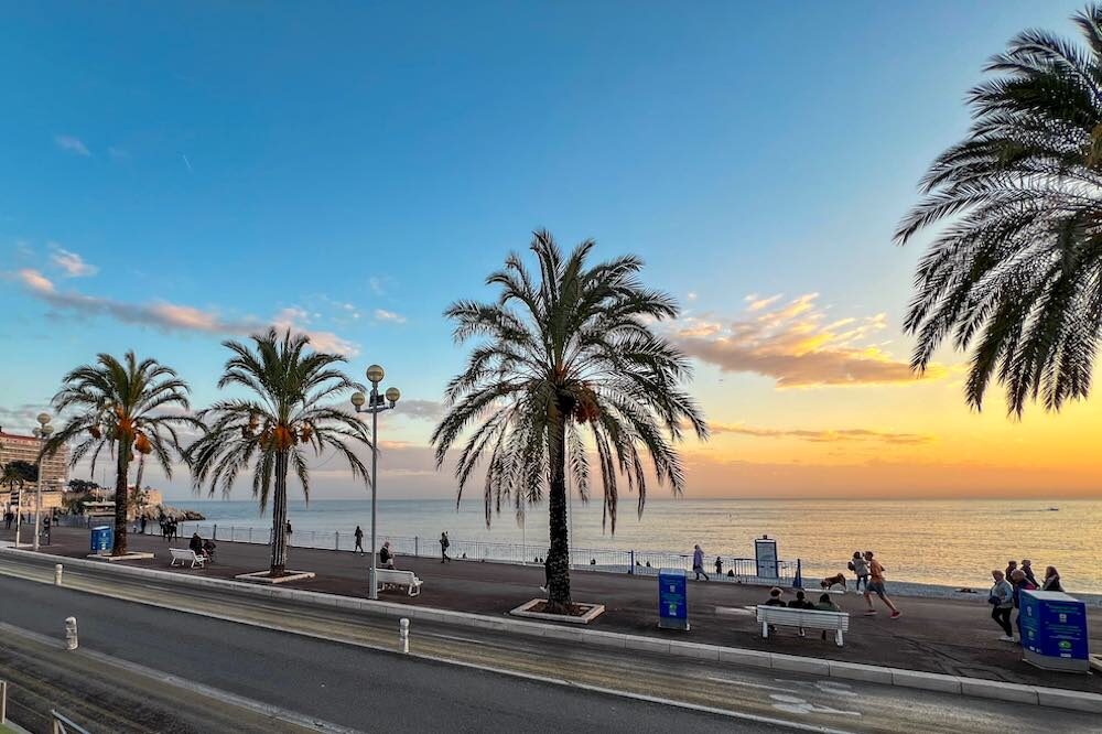 The Promenade des Anglais curving along the Baie des Anges at golden hour, cyclists on the seafront path.